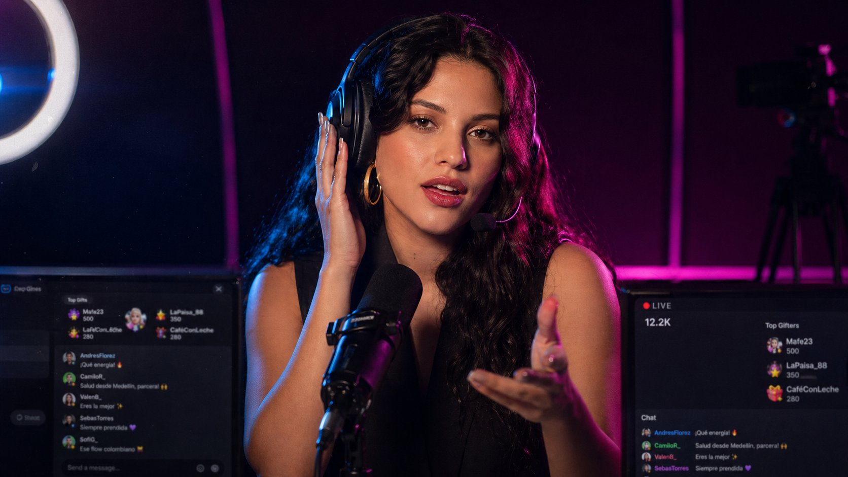 A Colombian livestream MC at her professional broadcast desk, wearing studio headphones and speaking to her global audience.